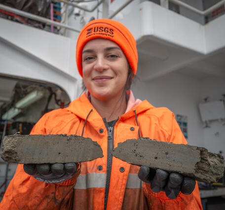 A person in an orange hat and jacket smiles towards the camera while holding rocks