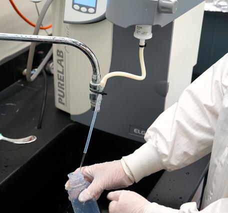 Scientist rinsing white plastic Teflon sample bottle with deionized water in a laboratory