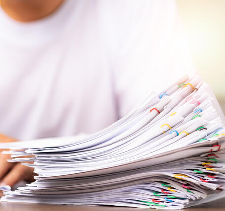 a man in a white shirt signs a paper with stack of paper clipped papers next to his hands