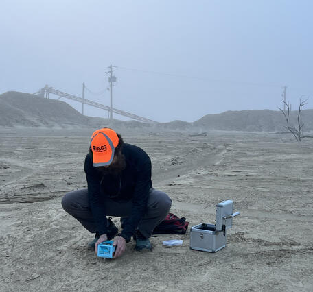 A man wearing an orange cap holds a device just above the ground to gather mine waste geophysical data