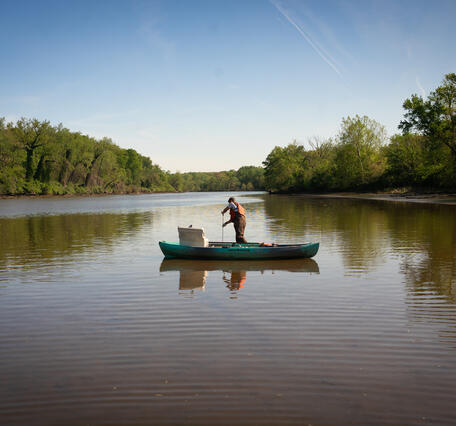 A hydrologic technician takes a water sample from a canoe.