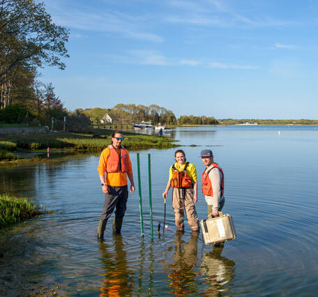 3 USGS employees stand in shallow water while installing monitoring equipment at Cape Cod