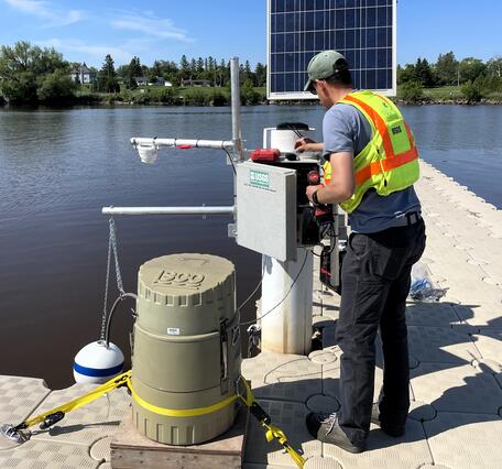USGS hydrologic technician installs equipment inside streamgage housing on shore of lake