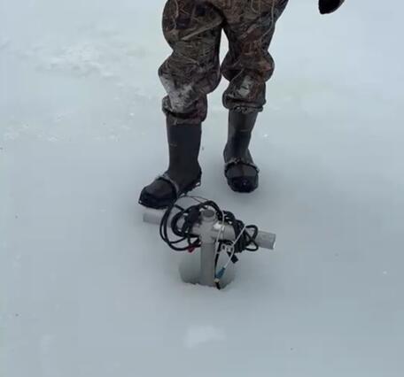 Scientist standing behind borehole in ice with an acoustic probe lowered