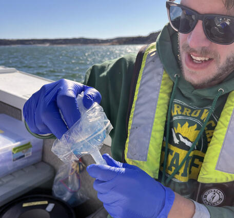 A man in a boat places a filter cap on eDNA equipment during sampling in a reservoir