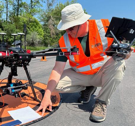 Matthew Burgess, kneeling before launchpad, prepares drone aircraft for flight