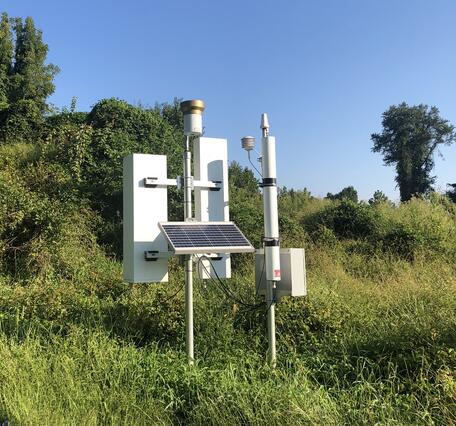 CRNS monitoring station on a grassy hillside with open blue sky overhead.