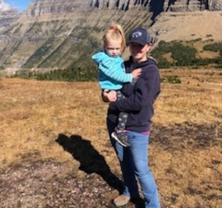 woman wearing baseball cap holding blonde child standing in front of desert background