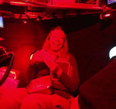 A red light glows over a person smiling and holding a sandwich 