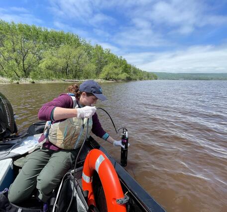 Scientist leans over side of boat to take water quality measurement with a sonde