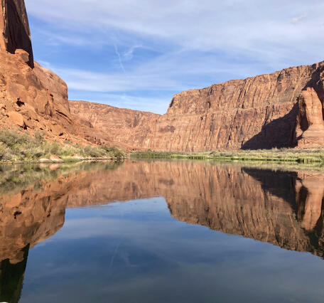 The Colorado River water reflects blue skies and red Grand Canyon walls