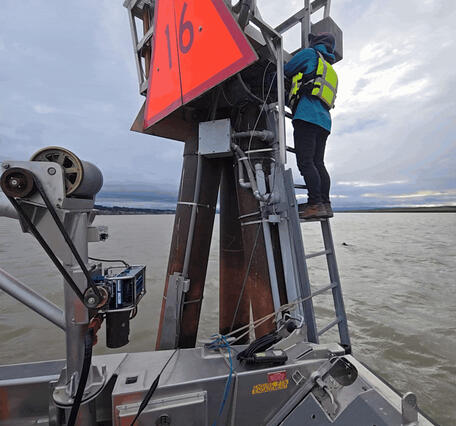 A technician climbs a steal dolphin to access gage equipment from a boat