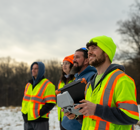 Four hydrologic technicians watch a small drone in the air (drone not in camera).