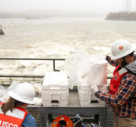 Standing on a catwalk, hydrologic technicians Kelly McVicker and Shane Mizelle prepare to collect water samples from the Conowingo Dam.