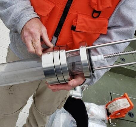 Scientist holds a transparent tube sediment corer device