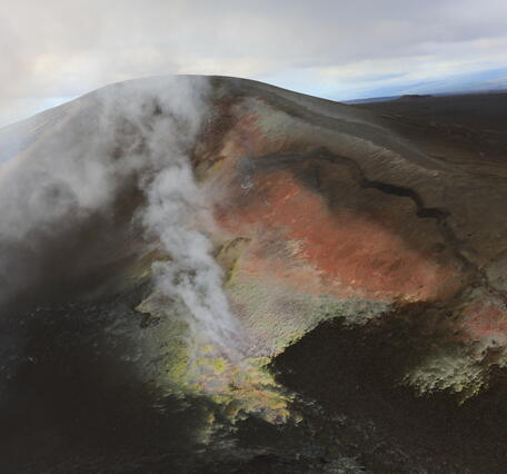 A brown hill of volcanic tephra with a crack and yellow and orange areas of alteration