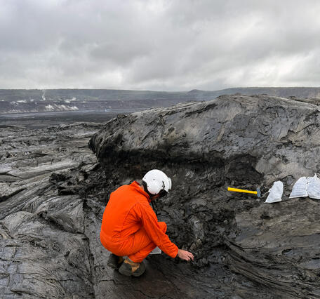 A scientist picking up pieces of lava from a lava flow surface