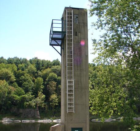 A four-story concrete tower stands next to the river, a ladder leading up to the landing platform