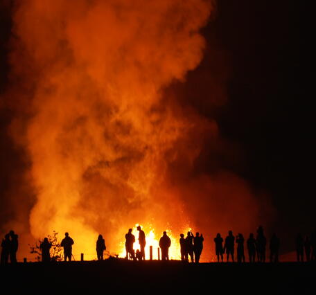 Silhouettes of people at night with a lava fountain and plume behind them