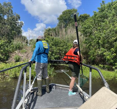 Two people in life jackets stand on a bow platform of a boat while electrofishing.