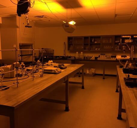 laboratory lit by dim amber-colored light, and with benches and cabinets that hold lab supplies and analytical equipment