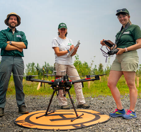 Three people standing behind a drone