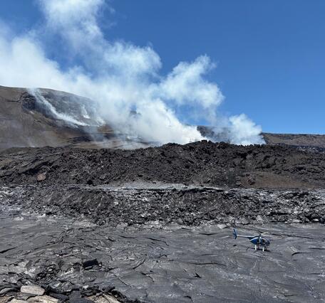 Color photo of black, cooling lava from the August 6th eruption episode 30 with the vents in the background.