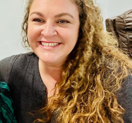 Headshot of a smiling woman with long, light brown curly hair.