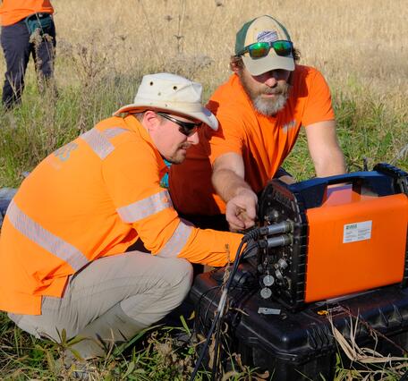Two scientists wearing orange, look at a mobile WalkTEM unit while in the field.