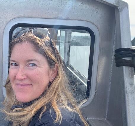 Elena Nilsen has blonde hair. She as sunglasses on her head and is smiling.