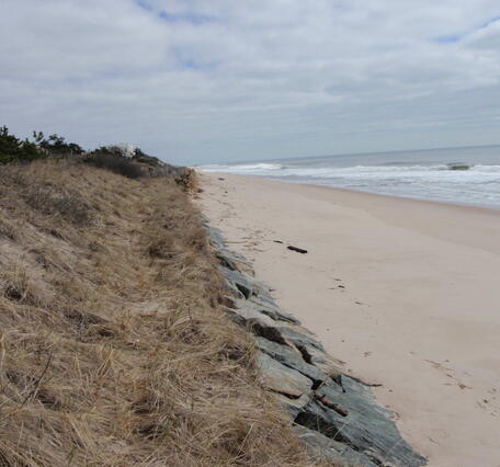 A human-made riprap rock seawall to protect an ocean dune at a beach is exposed by erosion