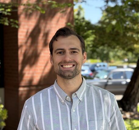 Staff photo of a man with short brown hair smiling in outdoors and wearing a collared shirt. 