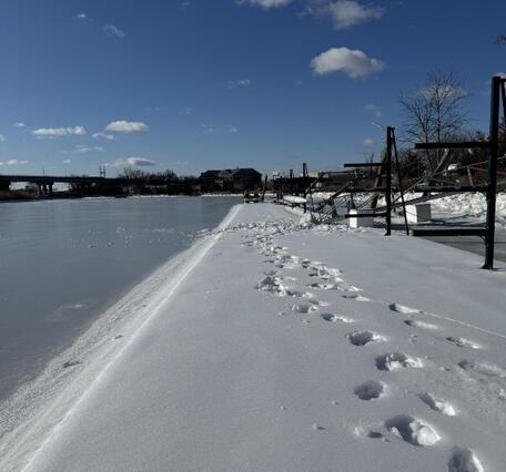 Footprints in snow next to a frozen river.