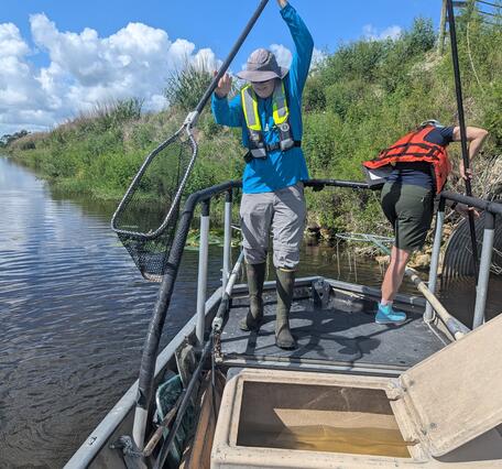 two people stand on a boat holding long nets