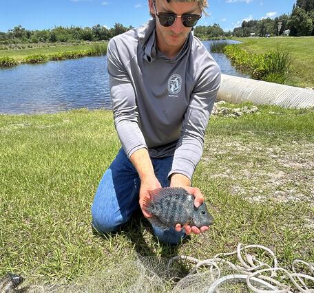 a man is shown holding a fish in front of a small body of water and a blue sky