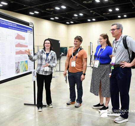 Four people standing to the right side of a geologic map poster. The person closest to the poster is gesturing towards it as they present the information.