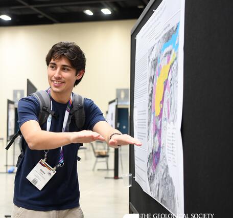 A student stands to the left of their geologic map poster gesturing towards it while presenting the information.