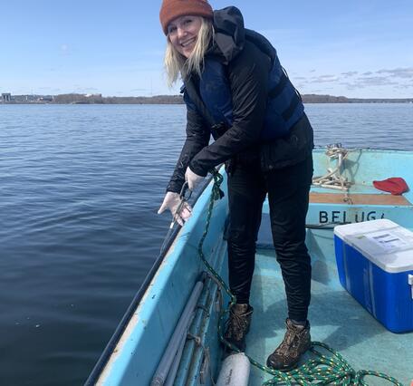 Woman smiling standing on bow of boat holding on to rope to sample water