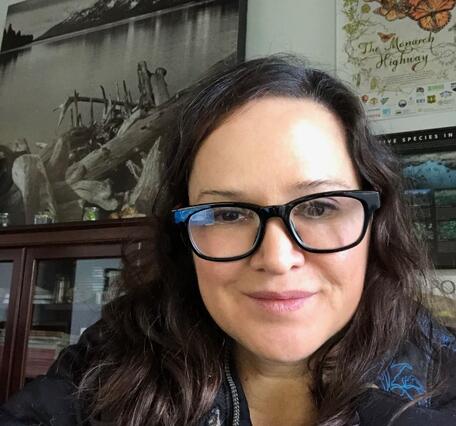 Headshot of a woman with long dark hair wearing glasses with a thick black frame