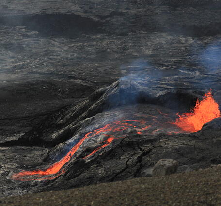 color photo of red hot lava flowing out of the vent, which is all black.