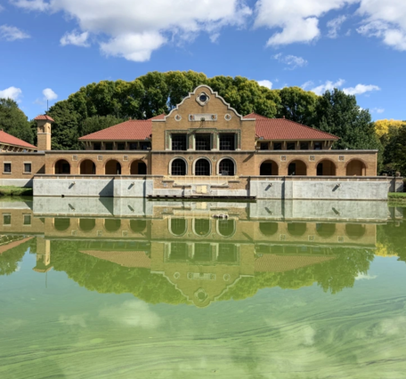 The Spanish Revival style Washington Park Lakehouse is reflected in murky green lake waters on a mostly sunny day