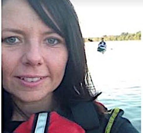 Womans face with brown hair and hazel eyes in front of a lake with a kayaker in it
