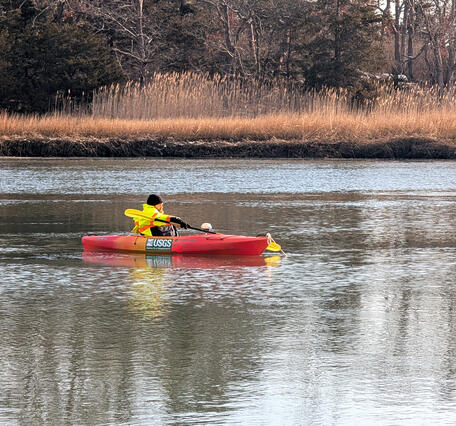 A man in a neon yellow jacket on an orange kayak in a river holding a paddle.