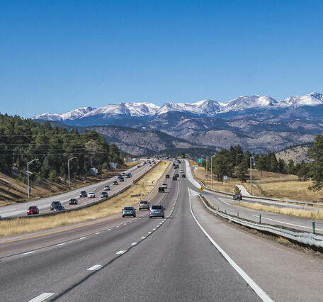 a four six lane road with frontage lanes with dozens of cars leading into snow-capped mountains