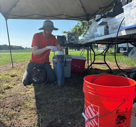 Scientist lowers a tape into a well with buckets and equipment waiting in the foreground