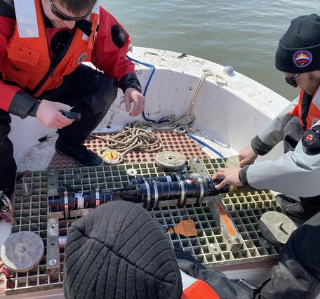Three people on a small boat working with a small piece of equipment