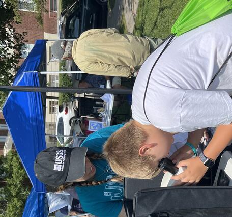Young person looking through microscope on a table outside.