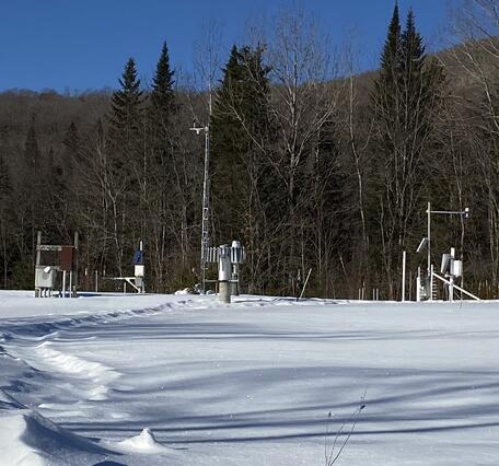Snow monitoring stations in a snowy field with woods in the background.