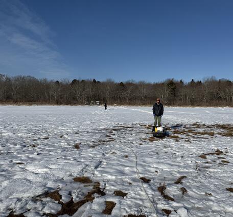 Scientist standing in coastal wetland in winter with snow on the ground