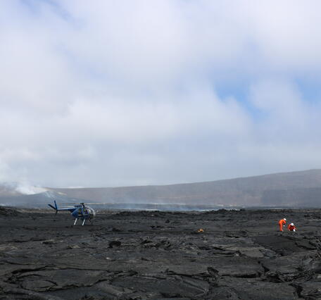 Color photograph of scientists working in volcanic crater with vent in background